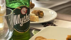 Græsk Mythos øl, populær øl fra Grækenland, forfriskende lys lager med mild smag, perfekt til varme sommerdage, serveres kold på tavernaer og strandbarer, brygget første gang i 1997, en af de mest kendte græske ølmærker, ideel til græsk mad som meze og grillet kød, oplevelser med lokal øl i Grækenland, must-try drik for ølelskere, tradition og moderne bryggeri kombineret, græsk ølkultur med international popularitet, nydes af både lokale og turister.