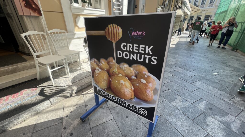 Græske loukoumades, traditionelle græske honningkugler, små friturestegte dejboller med sprød overflade og blød midte, overhældt med honning eller sirup og drysset med kanel og hakkede nødder, klassisk græsk dessert med rødder i antikken, serveres ofte ved festlige lejligheder og på markeder, populær street food i Grækenland, sødmefuld smag af Middelhavet, must-try græsk dessert for kageelskere, 