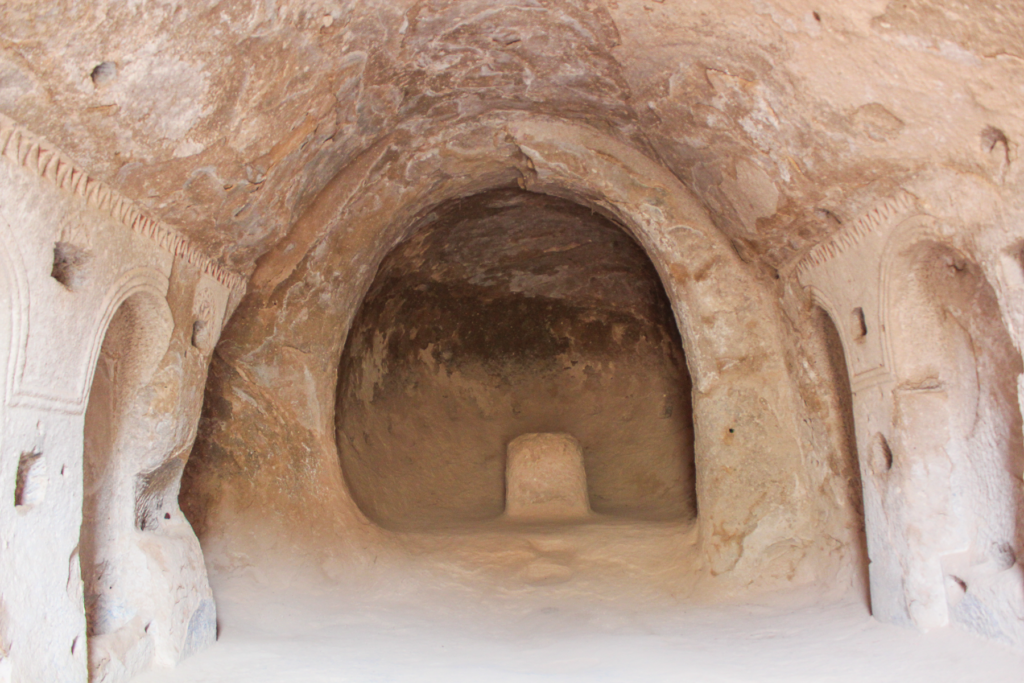 Den Hellige Kors Kirke i Zelve-dalen, klippeskåret kirke i Kappadokien, kristen kulturarv i Anatolien, helligdom i det vulkanske landskab, korsformede udskæringer i klippens vægge, tidlig kristendom i det centrale Tyrkiet, skjult kirke i Zelve Open Air Museum, religiøse motiver og enkle dekorationer, kirkerum i naturens stilhed, historiske oplevelser i Cappadocia, tro og tradition i klippehuler, seværdigheder i Zelve-dalen, autentisk atmosfære og byzantinsk arv i Kappadokien.