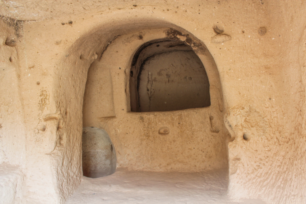 Den Hellige Kors Kirke i Zelve-dalen, klippeskåret kirke i Kappadokien, kristen kulturarv i Anatolien, helligdom i det vulkanske landskab, korsformede udskæringer i klippens vægge, tidlig kristendom i det centrale Tyrkiet, skjult kirke i Zelve Open Air Museum, religiøse motiver og enkle dekorationer, kirkerum i naturens stilhed, historiske oplevelser i Cappadocia, tro og tradition i klippehuler, seværdigheder i Zelve-dalen, autentisk atmosfære og byzantinsk arv i Kappadokien.