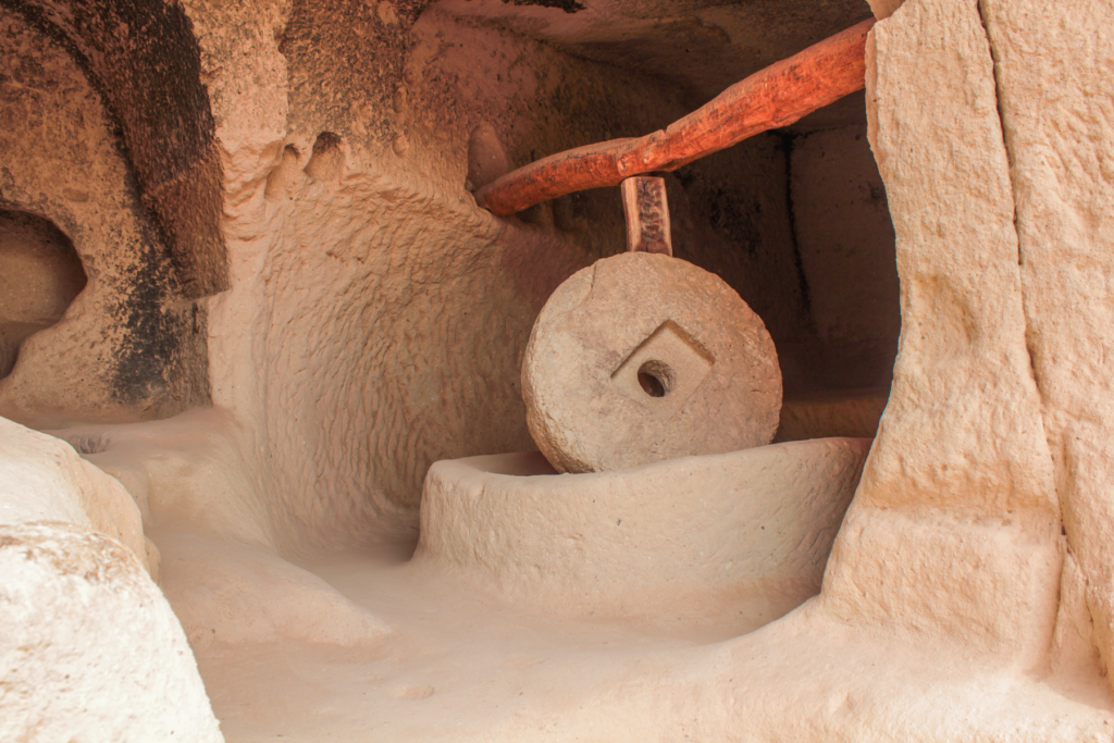 Møllesten i Zelve-dalen, seten i Kappadokien, historisk kornkværn hugget i klippen, dagligliv i hulebyerne, levn fra liv og arbejde i Zelve, stenredskaber brugt af beboerne, anatolsk kulturarv i Cappadocia, funktionelle huler med landbrugsværktøj, seværdigheder i Zelve Open Air Museum, autentiske detaljer fra det gamle liv, traditionelle møllesten i vulkansk sten, spor af hverdagsliv i klippeformationerne, unikke indblik i anatolsk historie og selvforsyning.